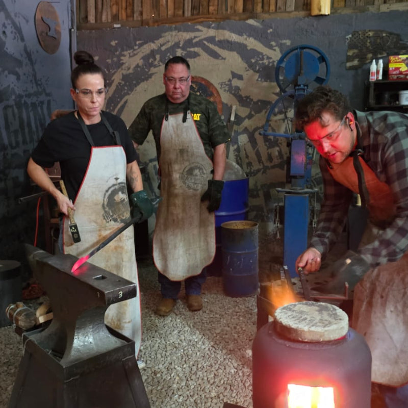 Three people working with hot metal in a forge setting