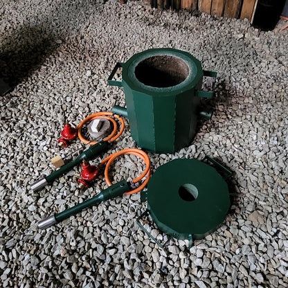 A black metal smelting furnace with two burners, hoses, and a foundry lid laid out on the floor.