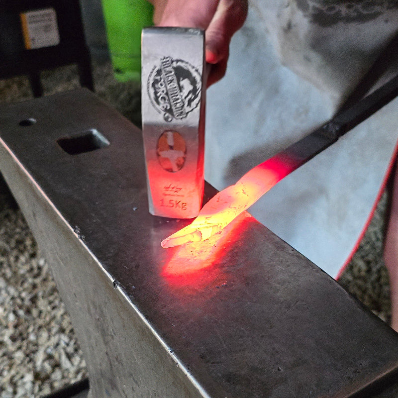 Person working with hot metal on an anvil in a workshop setting