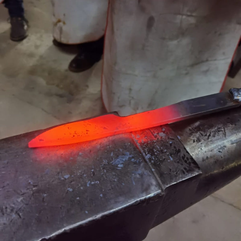 Red-hot metal blade on an anvil in a workshop setting