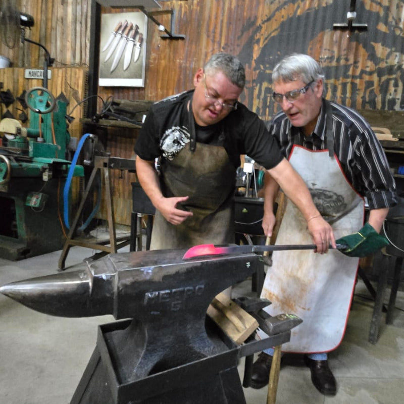 Two men working with metal during the Black Dragon Forge Bladesmithing Experience 