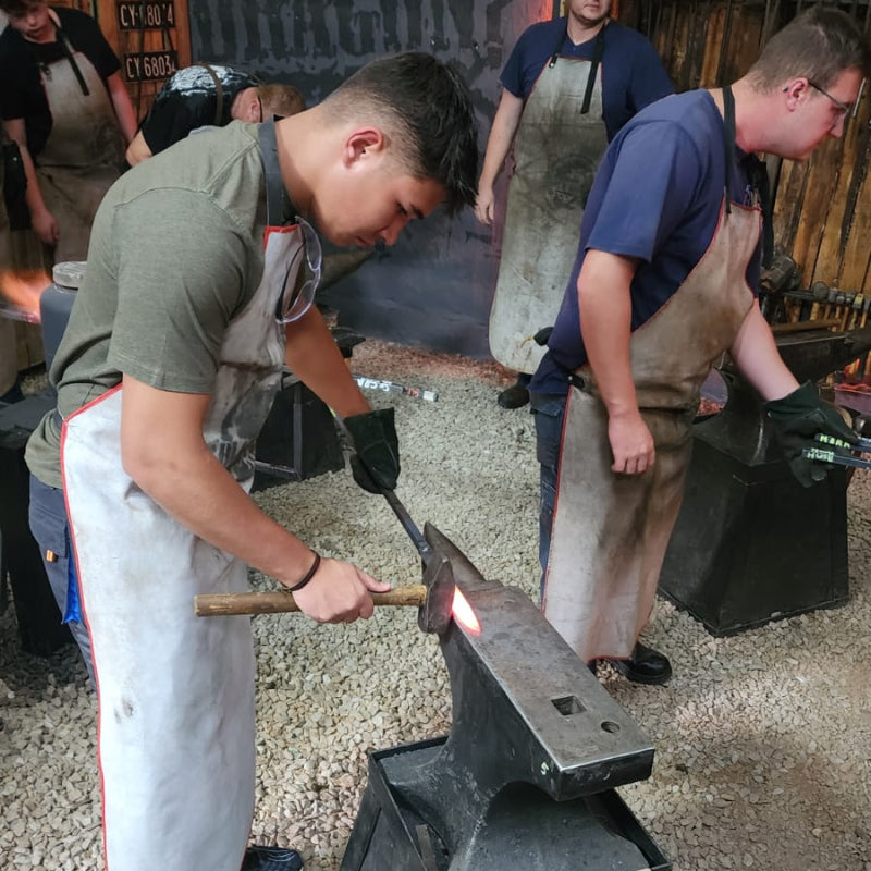 Two students working with a anvil and hammer in a Black Dragon Forge Bladesmithing Experience setting.