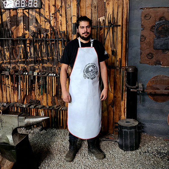 A person standing in a workshop wearing a white chrome leather apron with black buckles.