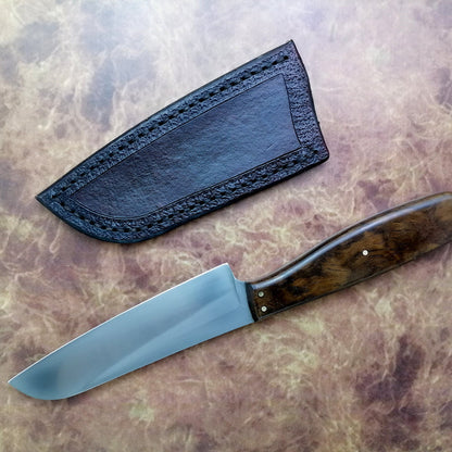 Knife with wooden handle and leather sheath on a textured surface