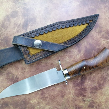 Knife with wooden handle and leather sheath on a textured surface