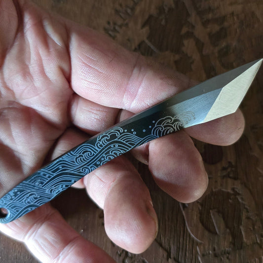 Hand holding a pocket knife with decorative handle on a wooden surface