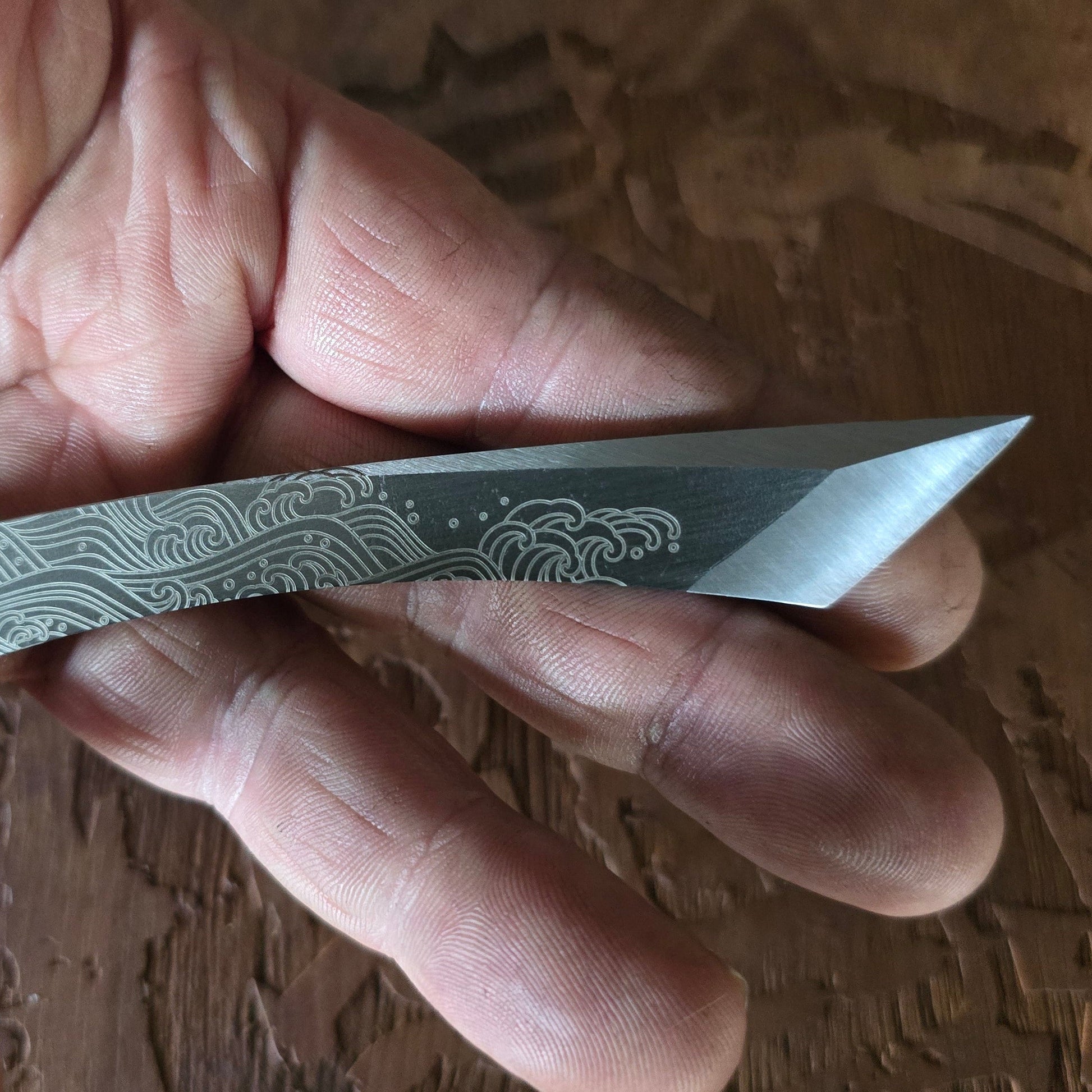 Hand holding a small pocket knife with a detailed blade against a wooden background