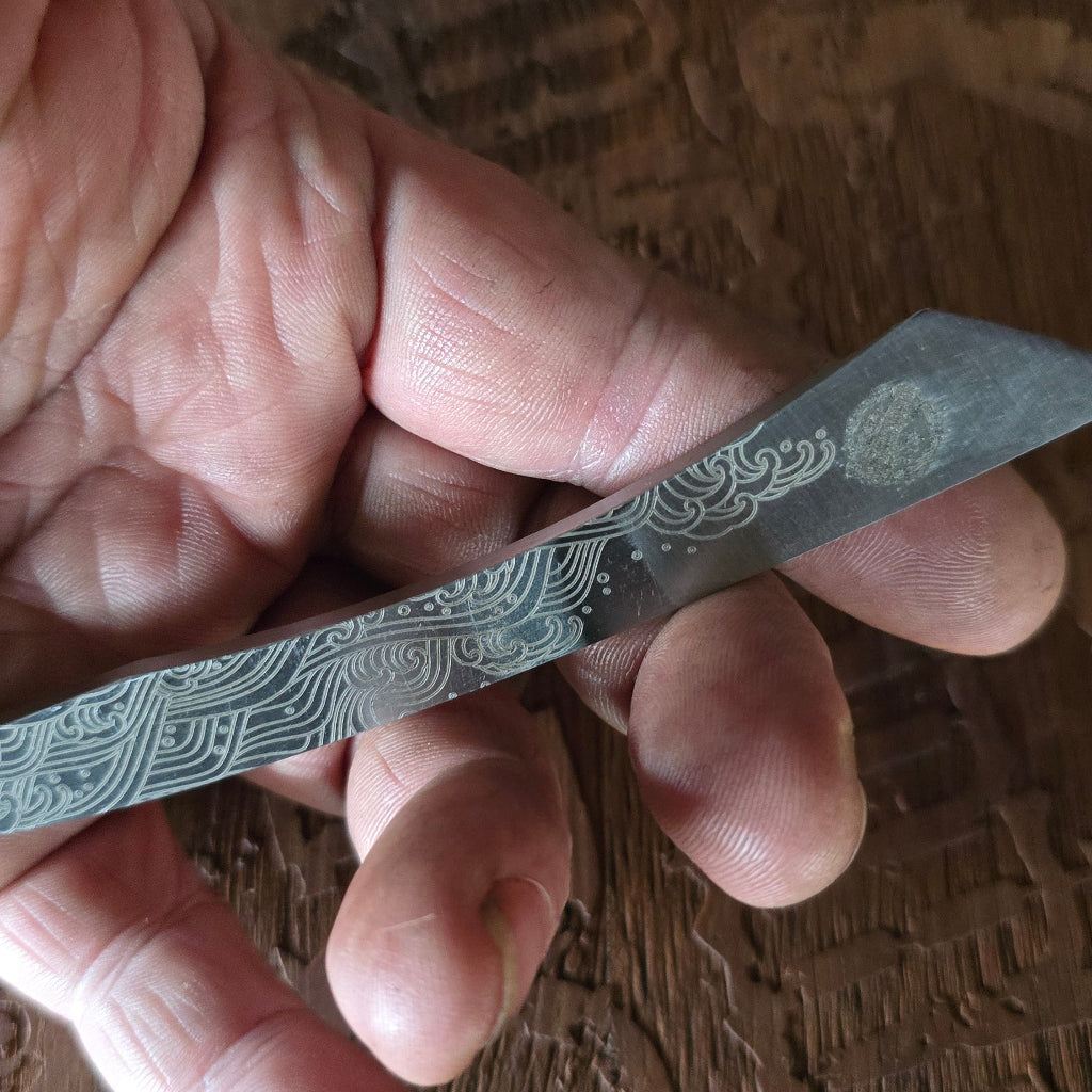 Hand holding a small pocket knife with intricate design on a wooden surface
