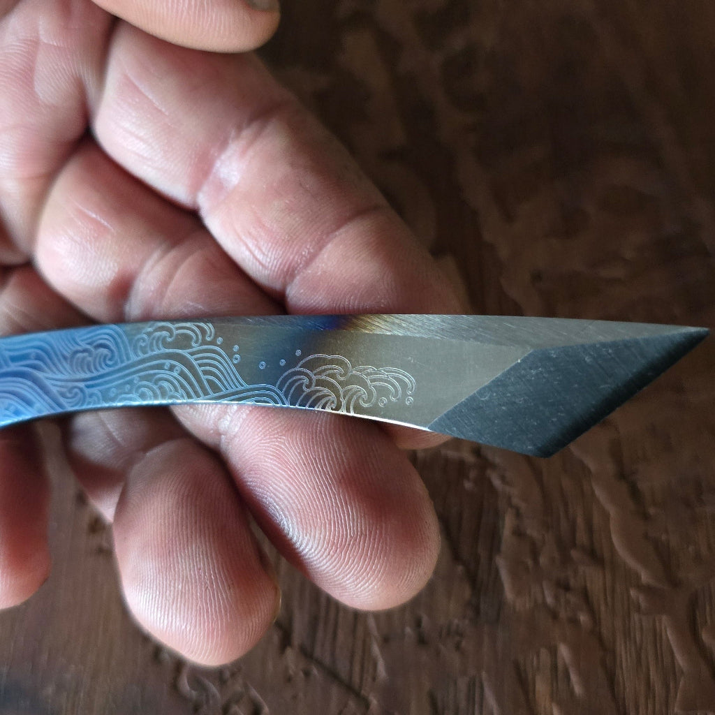 Hand holding a small knife with decorative blade on a wooden surface