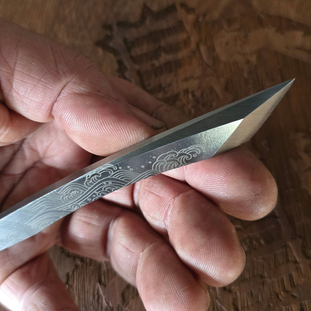 Hand holding a small knife with engraved design on a wooden surface