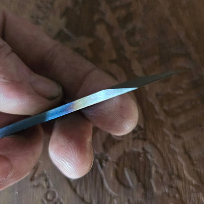 Hand holding a small metallic object against a textured wooden background