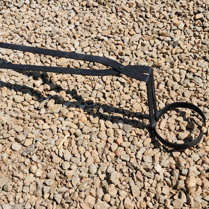 A pair of lift and pour crucible tongs made of mild steel, designed for handling a crucible, placed on a gravel surface.