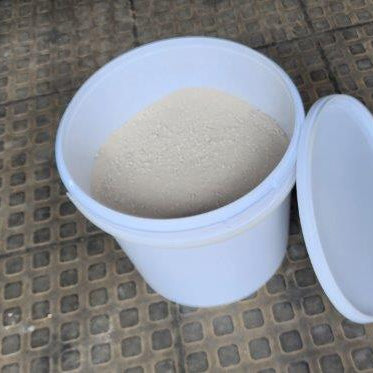 An open plastic container filled with white refractory cement, placed on a textured surface.