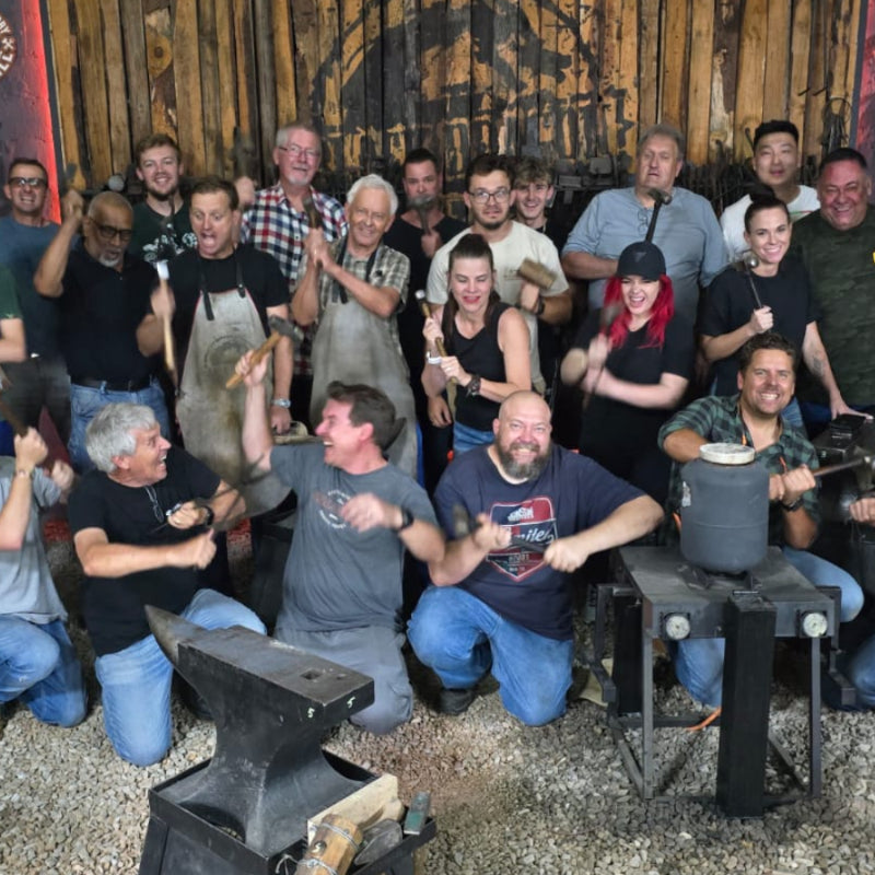 Group of people posing together in a workshop setting with an anvil and tools.